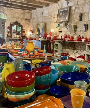 Kleurrijke keramische serviezen en decoratieve voorwerpen in een rustieke winkel.