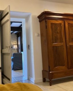 Een lichte kamer met een stoel, een spiegel en een open deur naar een andere ruimte.