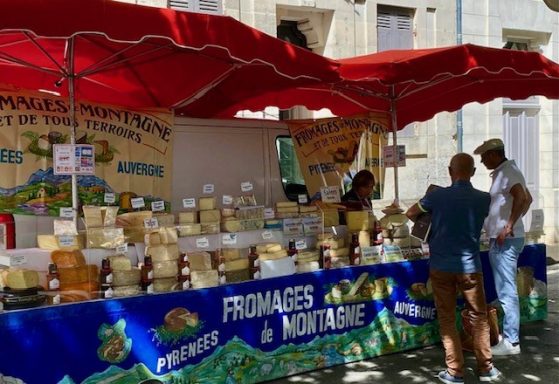 Kraam op een markt met verschillende soorten kaas en klanten die voor het aanbod staan.